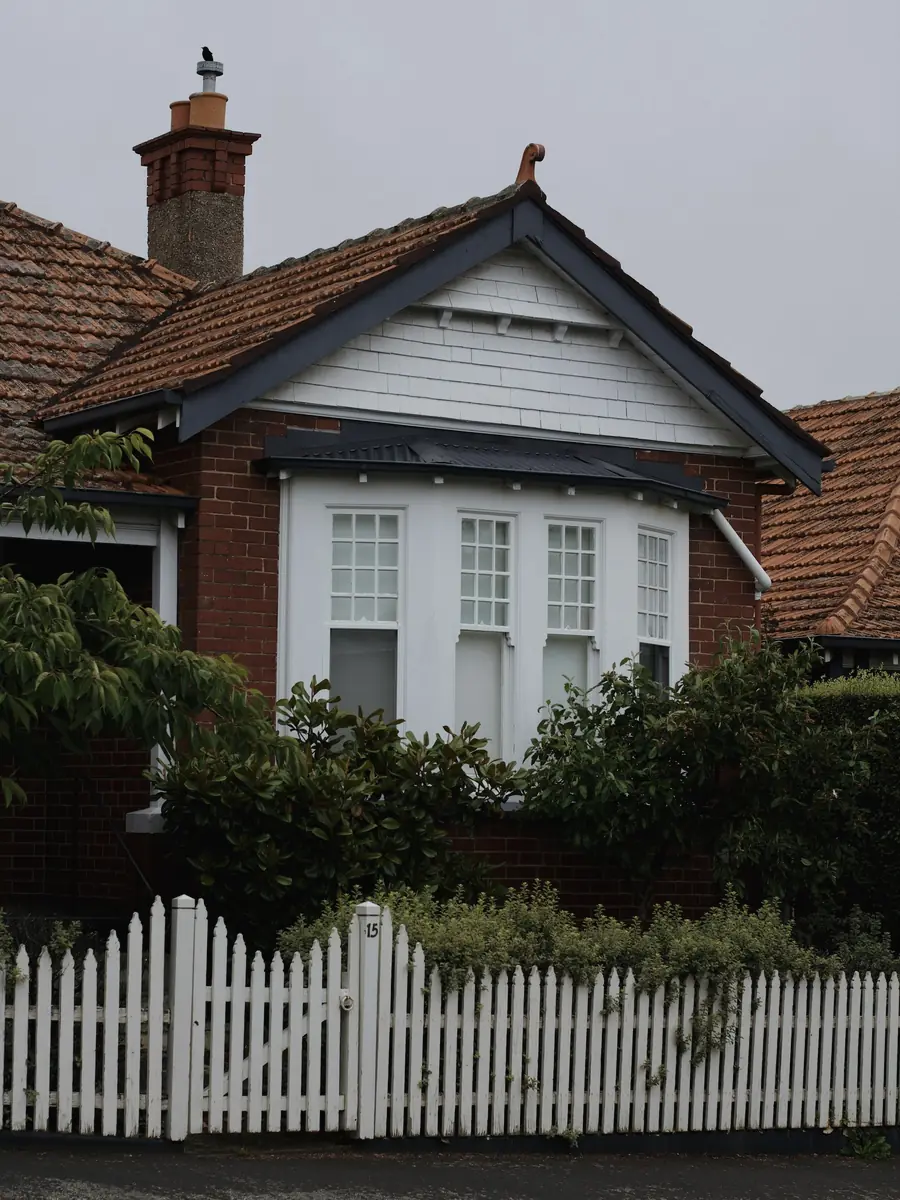 A red brick bungalow behind a white picket fence.